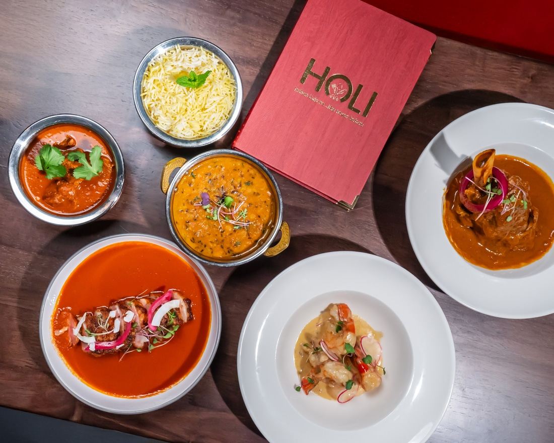 An overhead spread of curries, rice and breads on a walnut table at Holi